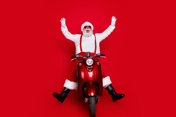 Obraz premium Santa Claus riding a red vintage scooter with arms raised, wearing sunglasses and white gloves celebrating Christmas and holiday fun against a bright red background