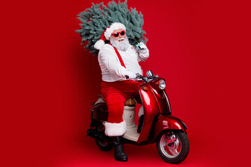 Obraz premium Santa Claus carrying a Christmas tree on a red scooter with sunglasses and festive outfit for holiday delivery and seasonal fun