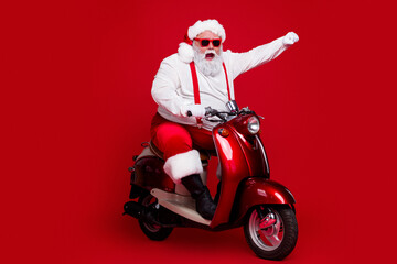Obraz premium Santa Claus riding a red scooter with sunglasses and raised fist, a festive Christmas character delivering playful holiday cheer against a bold red background