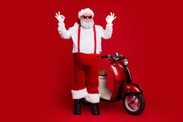 Obraz premium Santa Claus in red suspenders posing with a glossy red scooter for a festive Christmas holiday campaign