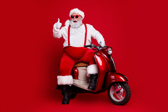 Santa Claus on a red scooter giving a thumbs up, wearing sunglasses and classic festive outfit against a bold red background for holiday fun