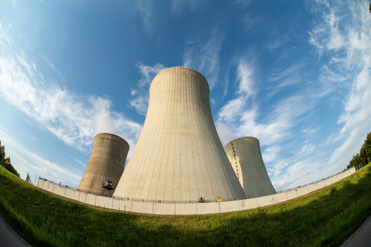 View of the large concrete cooling towers of a nuclear power plant under a bright blue sky with wispy clouds in Czechia.