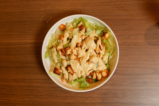 Top-down view of a classic Caesar salad served in a deep white bowl on a wooden table.