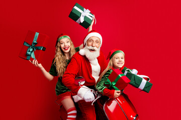 Obraz premium Santa Claus with two cheerful children on a red scooter holding wrapped gifts celebrating festive Christmas family joy