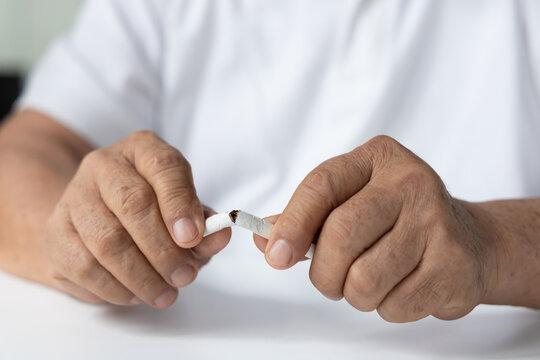 Elderly senior southeast asian man in his 70s breaking a cigarette at home, feeling sick and regretful about smoking indoors, concept image for quit smoking or stop smoking decision