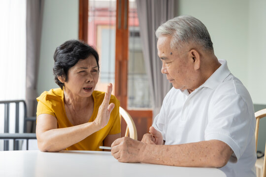 elderly southeast asian wife persuading her 70s husband to stop smoking indoors, concept image for quit smoking or stop smoking