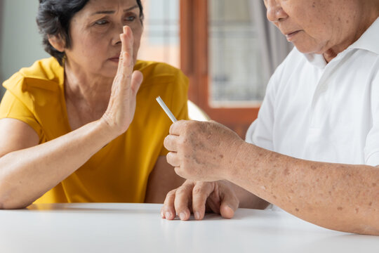 elderly southeast asian wife persuading her 70s husband to stop smoking indoors, concept image for quit smoking or stop smoking, hand closeup shot