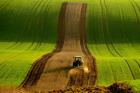 View of a tractor plowing a field in the rolling hills of Moravia in Brno-City District, South Moravian Region, Czechia.