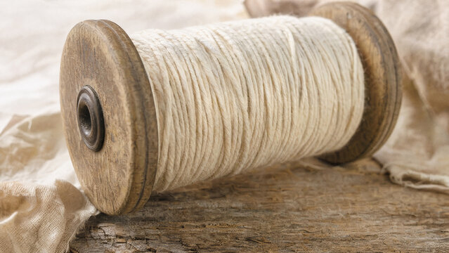 Natural unbleached cotton thread wound on vintage wooden spool on rustic surface