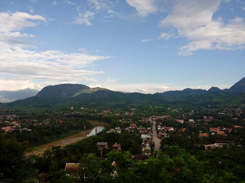​High angle view of Luang Prabang cityscape surrounded by tropical lush mountains and river, famous viewpoint at Phousi Hill, Laos.