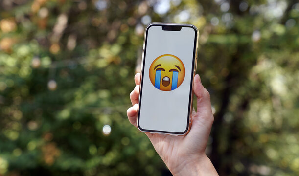 hand holding a smartphone with crying emoji, the most popular emoji of 2026, internet communication, gen z, overwhelming joy, dramatic exaggeration