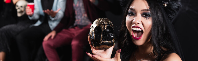 Obraz premium Excited asian woman celebrates Halloween with creepy skull, banner 