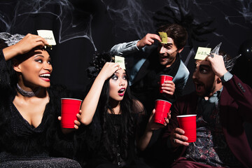 Obraz premium Multicultural friends enjoying a fun Halloween party and playing guess who game