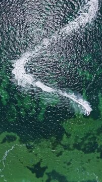 A jet ski moves quickly through clear blue green water leaving a white wake behind. The scene shows a bright sunny day at the beach with gentle waves.