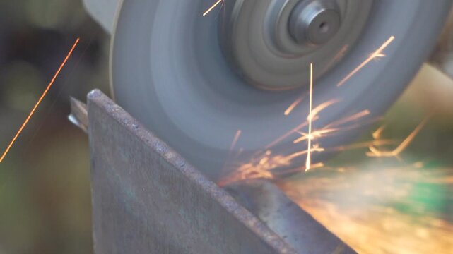 Metal surface friction occurs as an electric angle grinder cuts a steel plate in an industrial fabrication site. Macro tight shot.