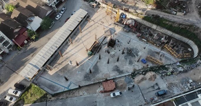 Aerial view captures the construction site, where a crane truck unloads steel reinforcements while workers organize the building area.