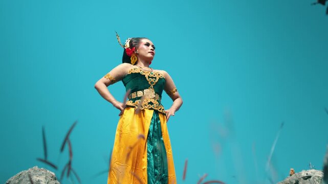 A dynamic low angle shot capturing a traditional dancer striking a pose on a hilltop, highlighting the colors against the blue sky.