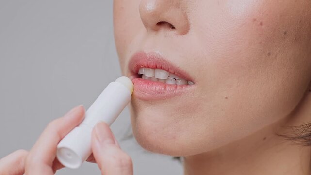 Focused Woman Applying Lip Balm To Moisturize Chapped Lips, Standing In Front Of Mirror At Home. Enhancing Beauty And Personal Care With Lip Moisturizer For Fresh Look. Skincare Concept.