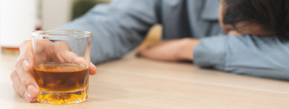Health care alcoholism drunk, fatigue asian young man hand holding glass of whiskey, alone depressed male drink booze on sofa at home. Treatment of alcohol addiction, suffer abuse problem alcoholism.