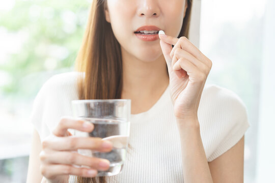 Dietary supplement, healthy positive asian young woman hand holding herb pill, take vitamin nourish body for treatment beauty skin, taking medicine with glass of water at home. Health care concept.