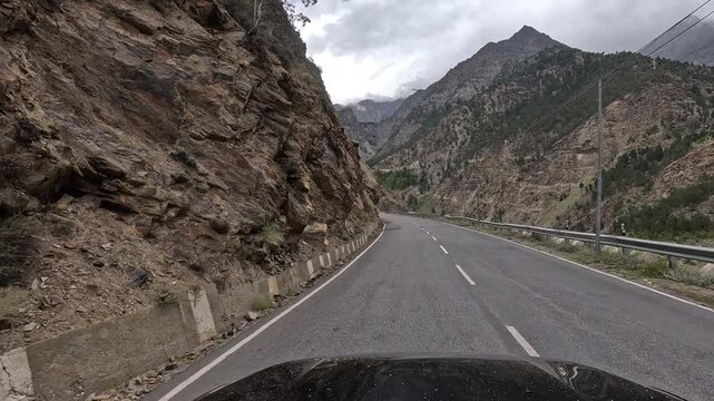 A vehicle drives along a paved mountain highway with concrete bollards past an exposed rock face cliff cutting with mountains an - Kinnaur Himachal Pradesh India | Himalayan road trip GoPro dashcam 4K