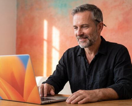 Contemplative mature architect with pencil behind ear working on laptop at wooden desk