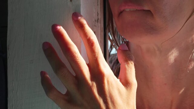Sultry gesture performed by tanned woman resting fingers against sunlit wooden frame. Close-up shot emphasizing texture, lighting, and intimacy.