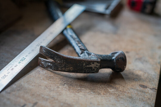 View of a weathered claw hammer and a metal ruler resting on a rustic wooden workbench in Looe, Cornwall, United Kingdom.