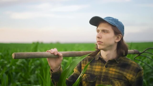Corn farmer pitchfork man. The young man stands in the green field, holding a hoe. The serene field and the man reveal a peaceful day in farming.