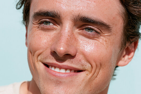 Young smiling man close up with radiant glossy skin, visible freckles, green eyes and natural expression in soft daylight