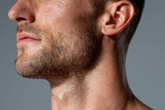Male jawline and neck glistening with sweat in close up portrait showing stubble beard and textured skin under directional light