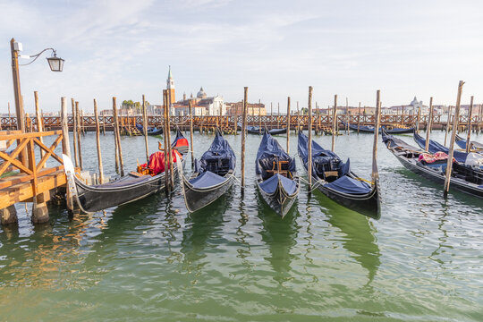 View of traditional gondolas moored to wooden posts in the calm waters of the lagoon with historic buildings in the background in Venice, Veneto, Italy.