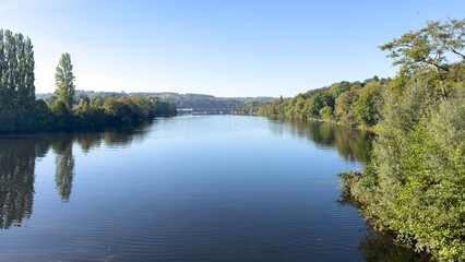 Obraz premium Wide landscape view across the Ruhr valley with calm water, woodland and a distant railway bridge.