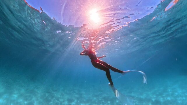 Underwater freediving adventure in turquoise tropical sea with bright sun rays filtering through surface. Vertical tracking shot.