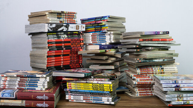 SOUTH KALIMANTAN, INDONESIA - SEPTEMBER 30, 2026: A large collection of Japanese manga comic books is neatly arranged in several tall stacks on a wooden table. The display features