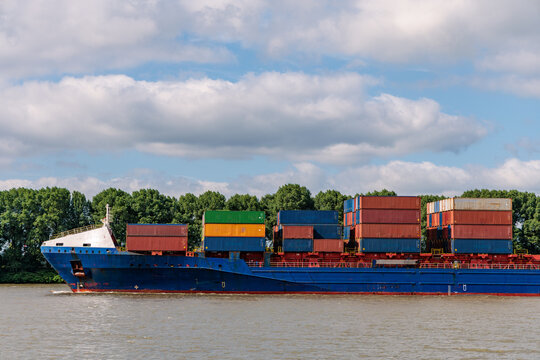 Blue container ship loaded with colorful stacked shipping containers sailing on the Elbe River in Hamburg, Germany, global trade, freight transport and logistics concept