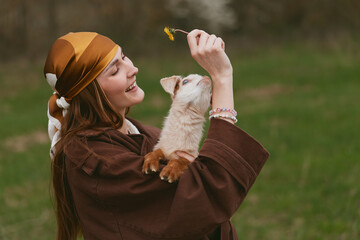 Obraz premium Smiling woman in a brown cloak embraces a playful goat kid outdoors, a warm lifestyle moment with nature, affection, and gentle light creating a cozy, intimate mood.