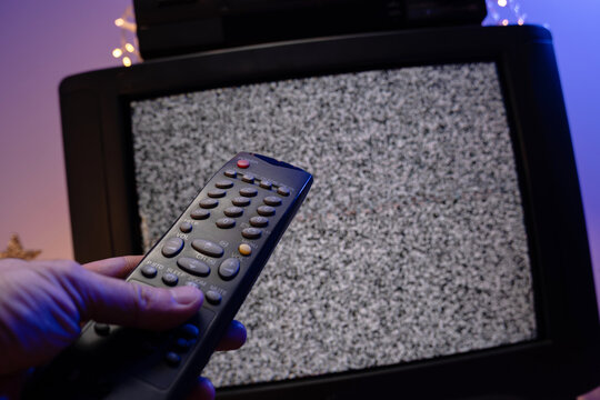 Hand holding television remote control in front of static noise screen