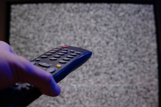 Hand holding television remote control in front of static noise screen