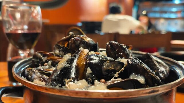 Close up of cooked mussels served in a pan with white wine in a restaurant setting.