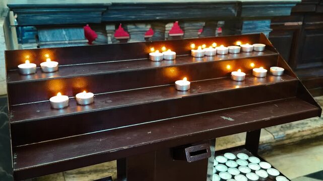Rows of small votive candles burning on a wooden candle stand inside a church, creating a warm atmosphere for prayer and reflection.