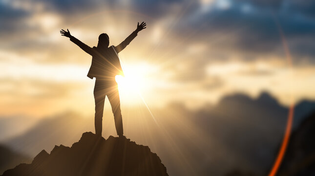 Silhouette showing successful businesswoman standing atop high mountain peak spreading arms wide toward glowing morning sunrise celebrating corporate victory outside among nature