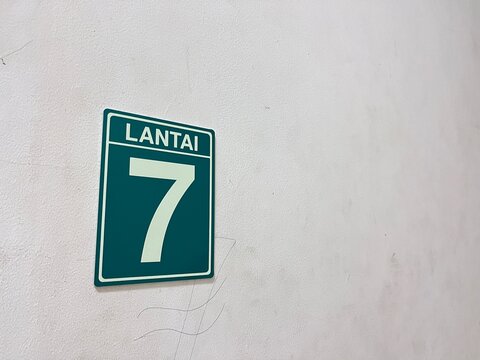 A green and white sign indicating the 7th floor, labeled 'LANTAI 7', mounted on a textured white wall