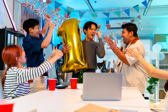Happy male employee holding gold number one balloon celebrating top sales achievement with colleagues in office party,business success,leadership,teamwork,business team and party new year concept