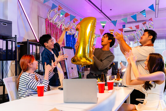 Happy male employee holding gold number one balloon celebrating top sales achievement with colleagues in office party,business success,leadership,teamwork,business team and party new year concept
