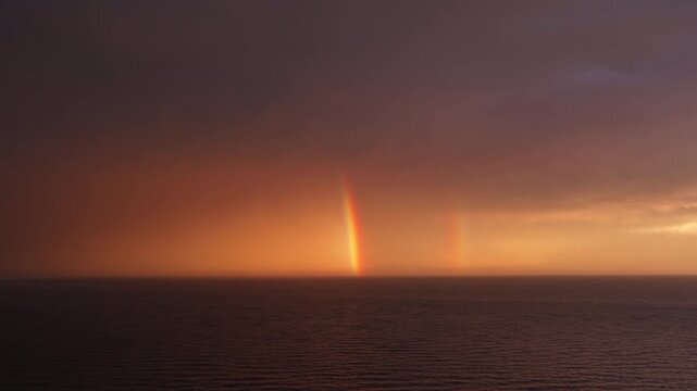 Double rainbow rising from the sea at orange sunset