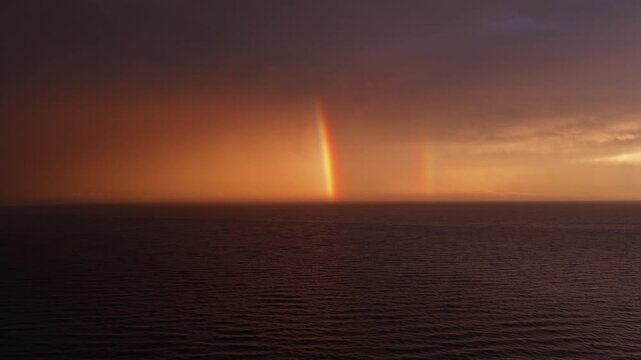 Bright sea rainbow under storm-lit orange dusk sky