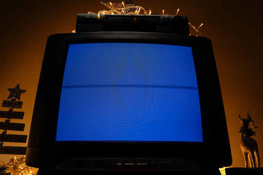Retro CRT television with VCR and Christmas lights, blue no signal screen in festive holiday interior