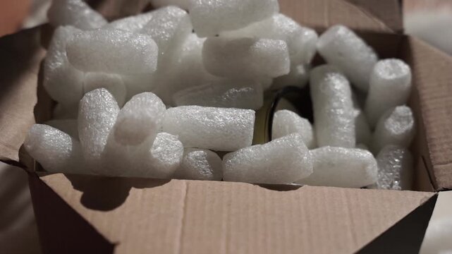 Pouring white biodegradable starch filler into a cardboard box with a glass candle for eco packaging of parcels. Box is filled with a filler safe for the environment that dissolves in water. 