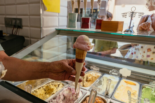 Fresh pink gelato in a waffle cone is held above the display counter, ready to serve to customers at a local ice cream shop in Spain.